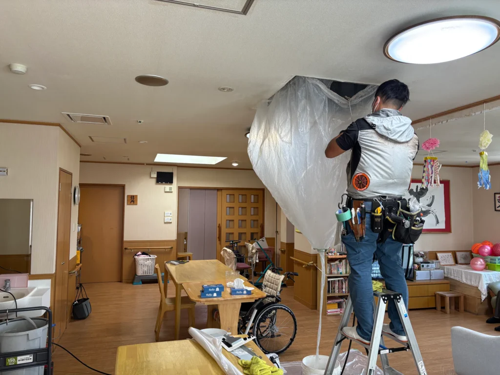 介護施設の室内で天井埋込型エアコンを洗浄する作業員
